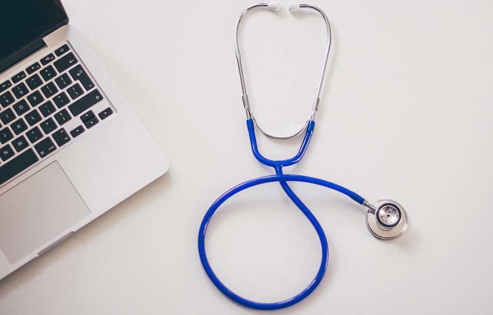 Corner of laptop and stethoscope on a flat surface