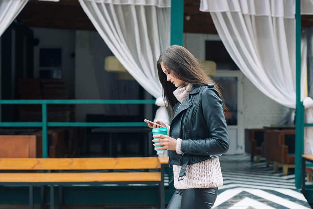 Woman texting and walking and holding travel mug