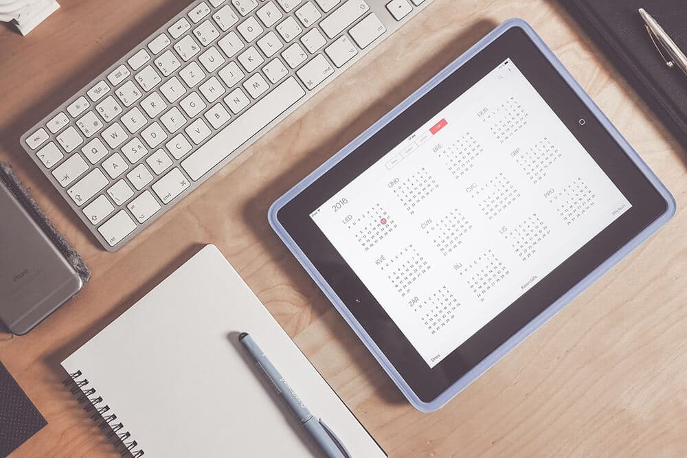 Desk with tablet showing calendar, keyboard, and notebook and pen