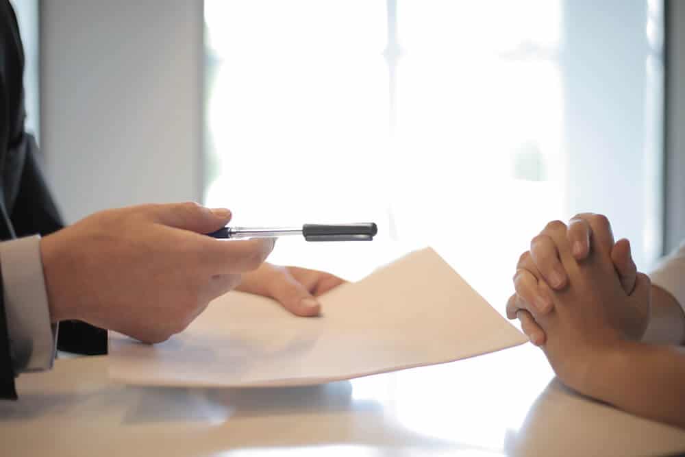 Person handing papers and pen to someone across the table 